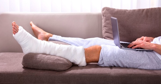 man with a broken leg, laying on the couch, typing on a laptop computer