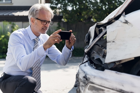 man taking a photo of the damage to a car after an accident